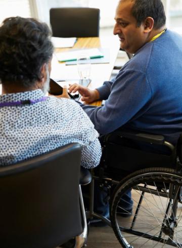 Homme d'affaires en fauteuil roulant discutant avec un collègue lors d'une réunion.